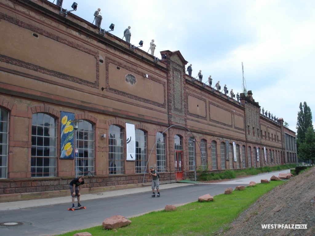 Fassade eines ehemaligen Gebäudes der Kammgarnspinnerei in Kaiserslautern. Die Figuren auf dem Fassadenabschluss waren Teil einer zeitweiligen Kunstinstallation und sind heute nicht mehr zu sehen.