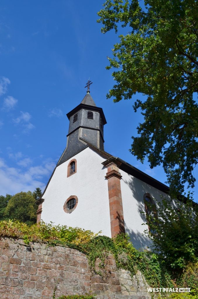 Westansicht der Rochuskapelle in Kaiserslautern Hohenecken. Links daneben ist eine Jesusfigur an einem großen Steinkreuz zu erkennen.
