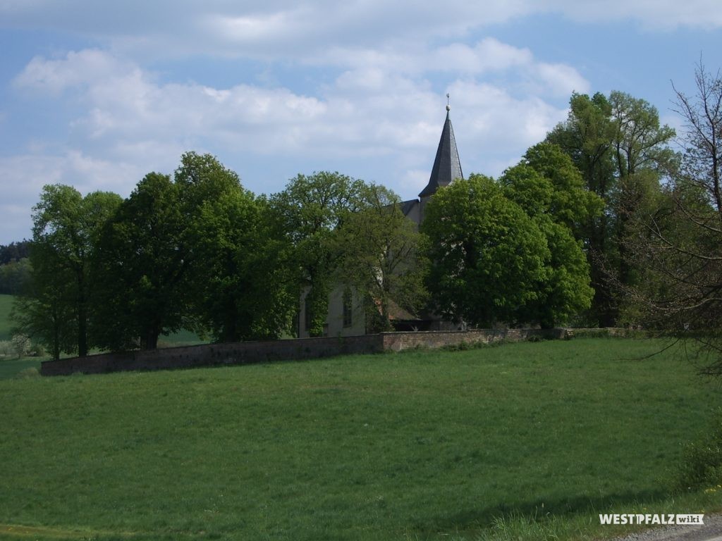 Flurskapelle in Ulmet hinter großen Laubbäumen sowie die die Kapelle umgebende Mauer