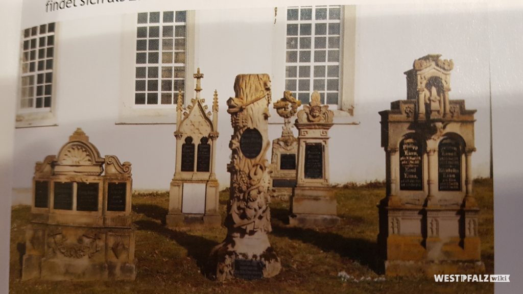 Historische Grabsteine zu Sitters. Im Hintergrund die Südwestfassade des Langhauses der protestantischen Kirche