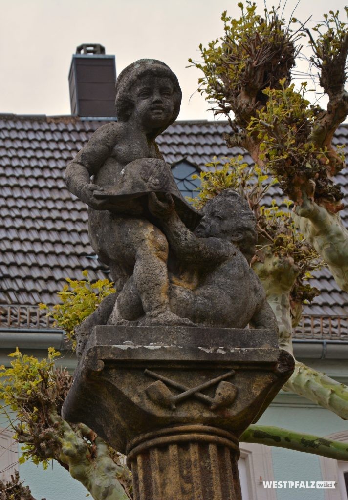 Figuren auf der Säule des Hutmacherbrunnens in Kusel. Zu sehen sind zwei spielende Kinder mit einem Schiffshut in den Händen