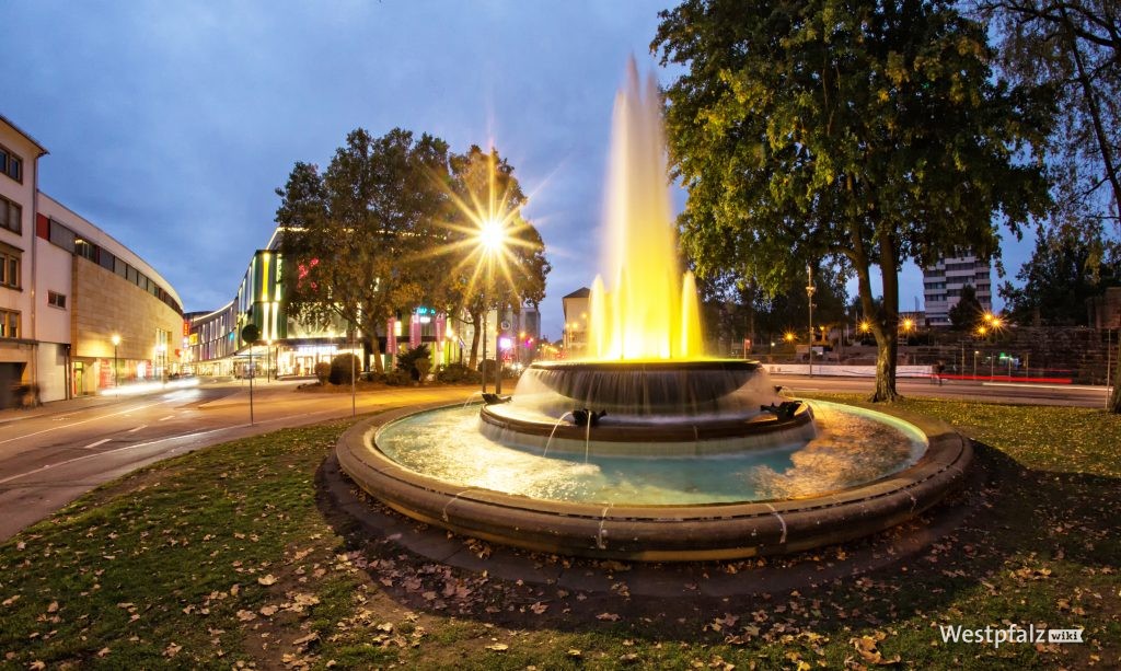 Der Fackelbrunnen am Abend. Im Hintergrund das Rathaus und das Einkaufszentrum.